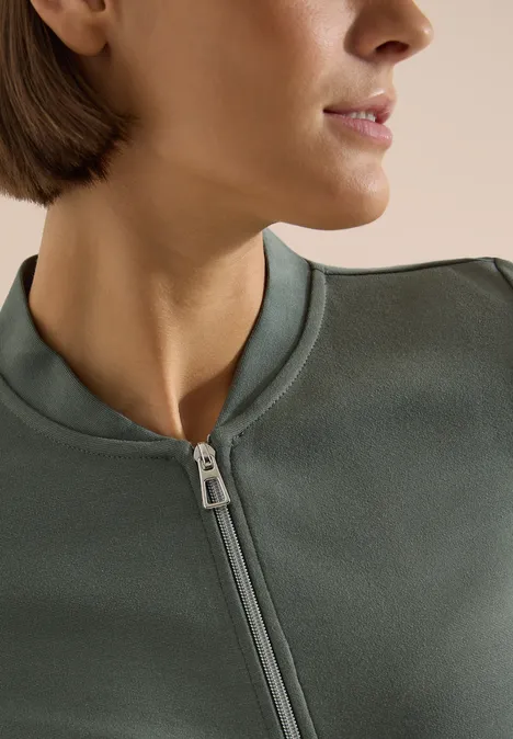 Langarm Jacke mit Rundhals und Zipper dried olive green Nahaufnahme einer seitlichen Ansicht einer Person in einem olivgrünen, hochgeschlossenen Reißverschluss-Pullover.