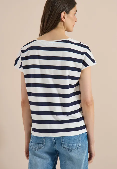 Vrouw van achteren in wit T-shirt met blauwe strepen en jeans voor een beige achtergrond.