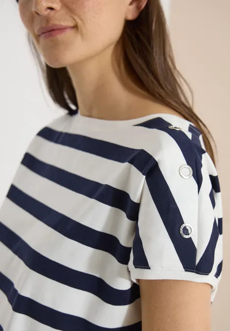 Vrouw draagt wit-blauw gestreept shirt met korte mouwen en zilverkleurige ringen op de schouder