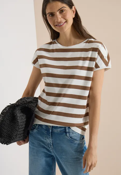 Vrouw in bruin-wit gestreept T-shirt en spijkerbroek met zwarte strooien tas