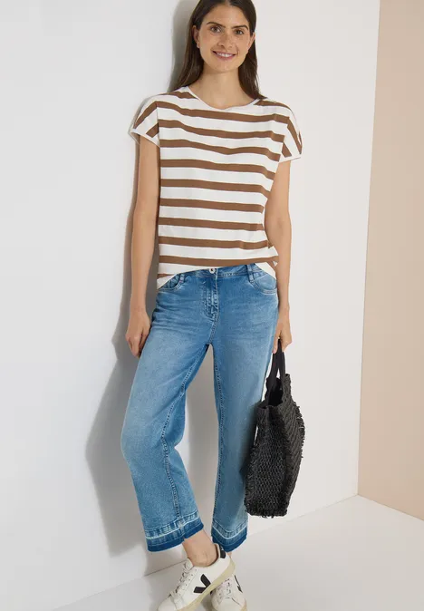 Vrouw in gestreept shirt, wijd blauw spijkerbroek en witte sneakers, met een zwarte, zachte shopper.