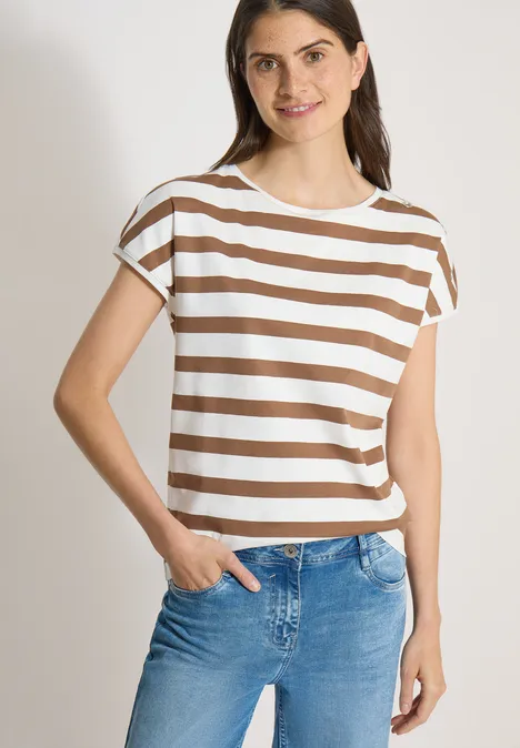 Vrouw met een wit-beige gestreept kort shirt en blauwe jeans, één hand in de zak.