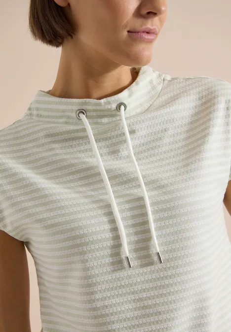 T-Shirt mit Funnel Neck und Streifen raw matcha lime Frau trägt hellgrau-weiß gestreiftes Top mit hohem Kordelzug-Kragen.