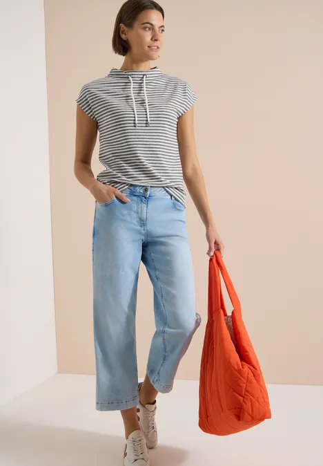 T-shirt à col cheminée et rayures urban dark blue Modische Frau in gestreiftem Kapuzenshirt, weiten Jeans, weißen Sneakern und orangefarbener Tasche.