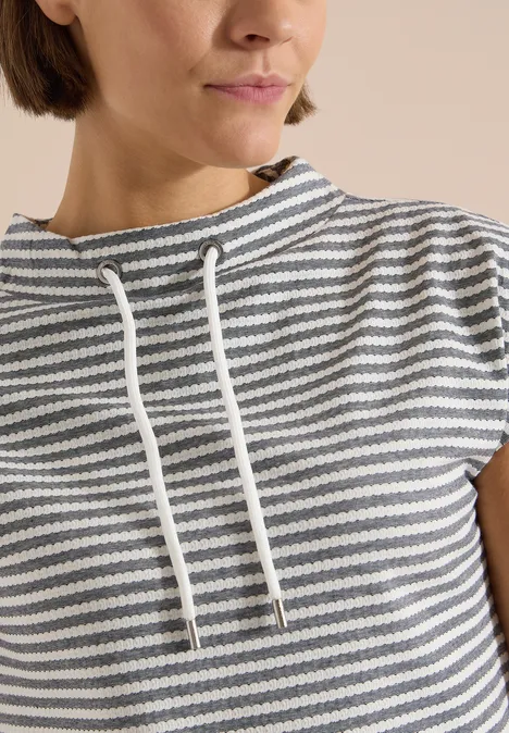 T-shirt à col cheminée et rayures urban dark blue Frau trägt grau-weiß gestreiftes Kurzarmshirt mit lockerem Kordelkragen.
