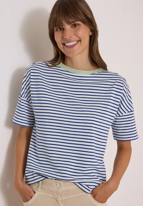 Eine lächelnde Frau in gestreiftem T-Shirt, die die Hände in die Taschen steckt.