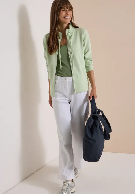 Langarm Jacke mit Ottoman Struktur raw matcha lime Frau in grüner Strickjacke, weißer Hose und großer blauer Tasche vor neutralem Hintergrund.