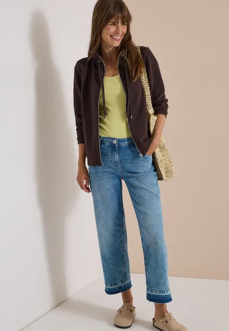 Langarm Jacke mit Ottoman Struktur truffle brown Frau mit dunkelbrauner Jacke, grünem Top, blauen Jeans, Korbtasche und Sneakers vor beige-weißer Wand.