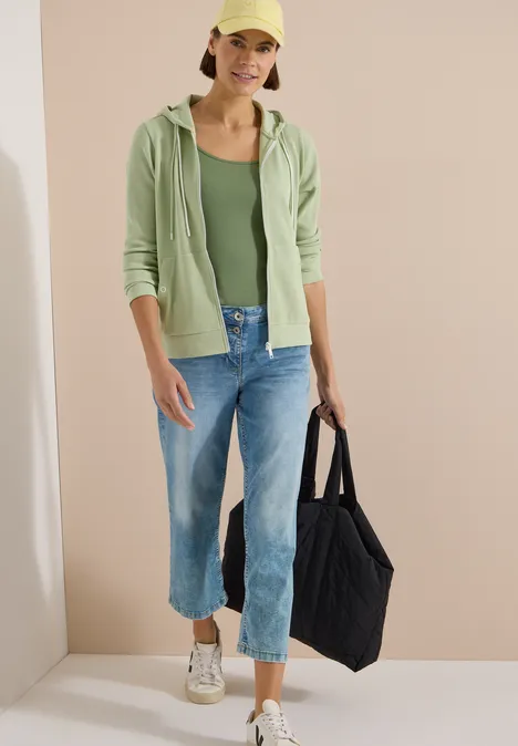 Langarm Jacke mit Kapuze und Struktur raw matcha lime Person trägt grünen Hoodie, grünes Top, weite Jeans und Sneakers, hält schwarze Einkaufstasche.