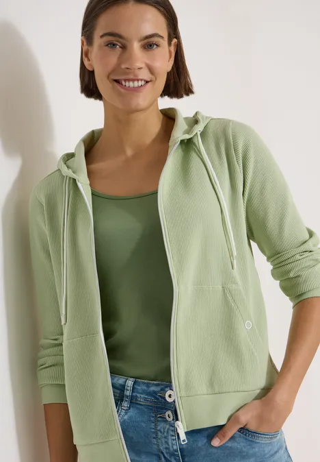 Langarm Jacke mit Kapuze und Struktur raw matcha lime Person in grüner Kapuzenjacke und Tanktop mit blauen Jeans vor hellem Hintergrund.