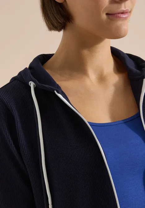 Langarm Jacke mit Kapuze und Struktur urban dark blue Frau trägt blaues Tanktop und dunkelblauen Kapuzenpullover mit Reißverschluss und weißen Kordeln.