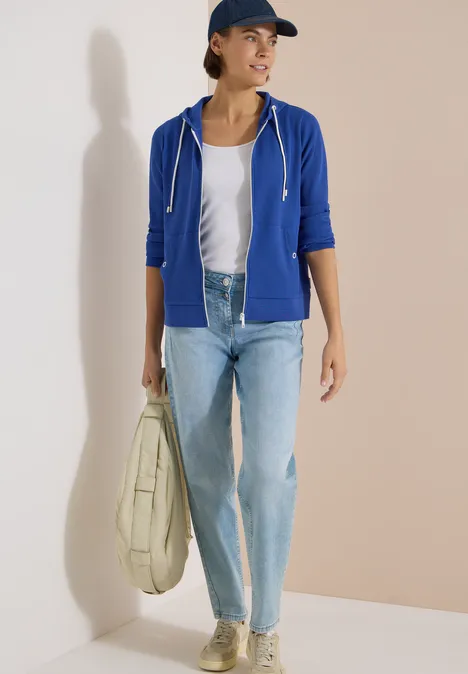 Langarm Jacke mit Kapuze und Struktur deep river blue Person mit blauer Kapuzenjacke, weißem T-Shirt, hellen Jeans, Sneakern und großer beiger Tasche.