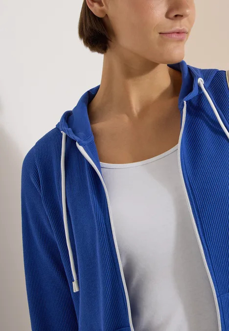Langarm Jacke mit Kapuze und Struktur deep river blue Teilansicht einer Frau mit weißem Top und blauer Kapuzenjacke, Fokus auf den Oberkörper