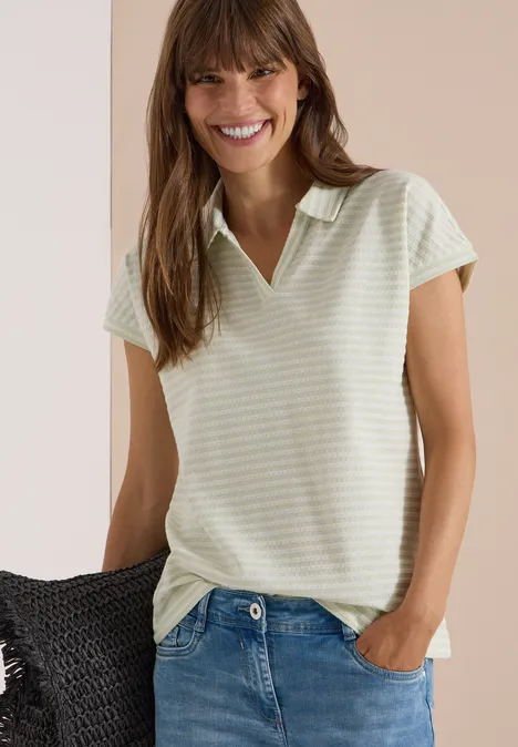 Kurzarm Poloshirt mit Streifenstruktur raw matcha lime Eine lächelnde Frau im gestreiften, hellgrünen Poloshirt mit V-Kragen und Jeans.