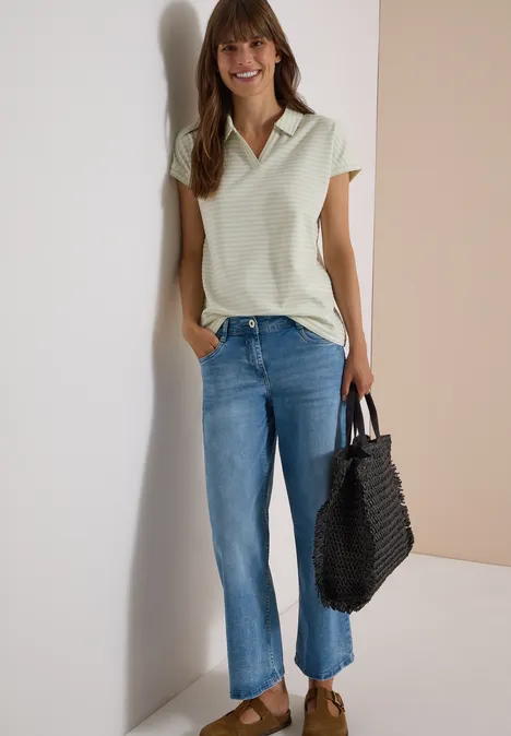 Kurzarm Poloshirt mit Streifenstruktur raw matcha lime Frau mit braunen Haaren trägt hellgrünes Top, blaue Jeans und schwarzen Korbtasche vor hellem Hintergrund.