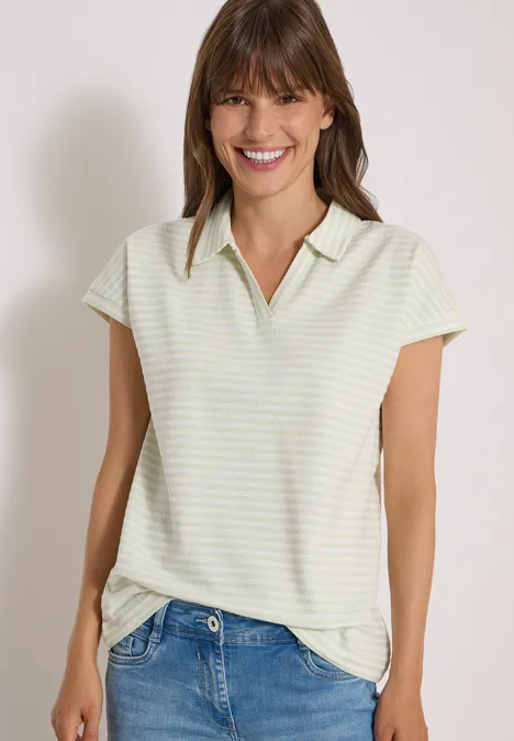 Kurzarm Poloshirt mit Streifenstruktur raw matcha lime Lächelnde Frau in gestreiftem kurzärmligem Poloshirt und Jeans vor hellem Hintergrund.