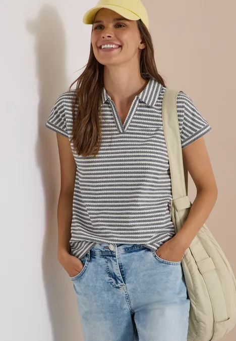 Kurzarm Poloshirt mit Streifenstruktur urban dark blue Frau in gestreiftem Poloshirt, Jeans, gelber Kappe und Umhängetasche lächelt.