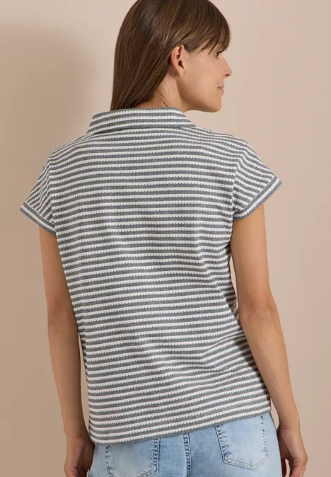 Kurzarm Poloshirt mit Streifenstruktur urban dark blue Frau steht seitlich, Rücken zur Kamera, trägt gestreiftes Kurzarmshirt und helle Jeans.