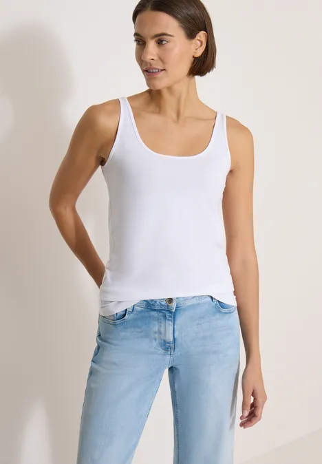 Haut long à col rond, de couleur unie White Frau in weißem Tanktop und hellblauen Jeans vor neutralem Hintergrund.