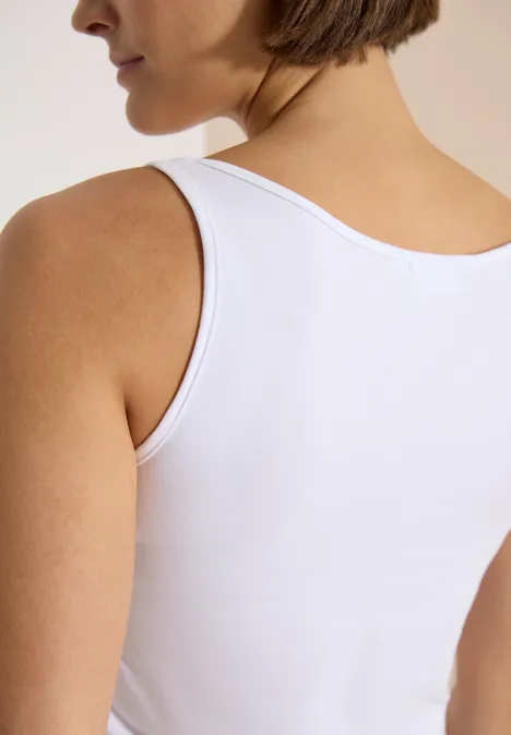 Haut long à col rond, de couleur unie White Seitliche Nahaufnahme einer Frau von hinten in weißem ärmellosem Oberteil.