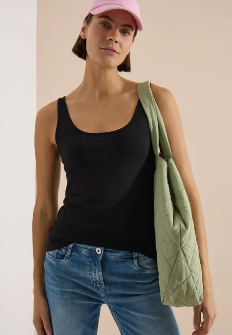 Frau in schwarzem Top, Jeans und grüner Umhängetasche, trägt rosa Cap.
