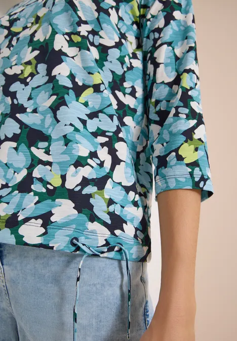 Damen-Oberteil mit 3/4-Ärmeln und blau-weißem Blumenmuster, vorne mit Bindeband, kombiniert mit Jeans.