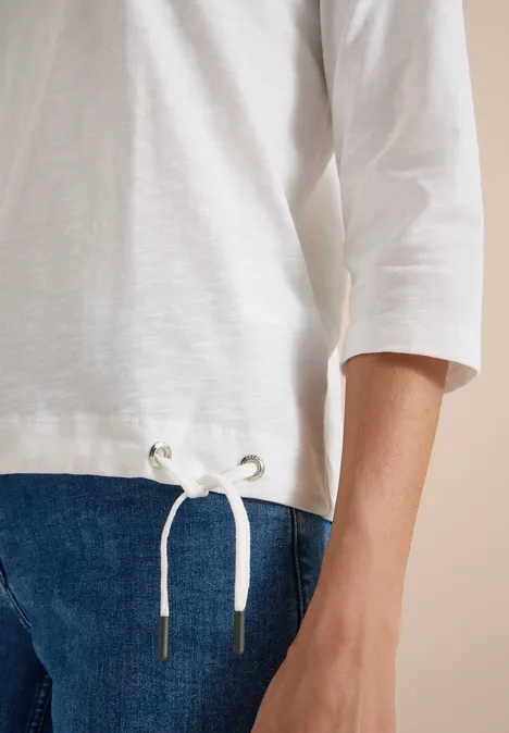 Eine Nahaufnahme eines weißen 3/4-ärmeligen Shirts mit Kordelzug und blauer Jeans.