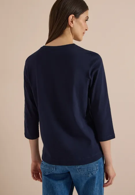 Rückansicht einer Frau in dunkelblauem 3/4-Arm-Shirt und Jeans.