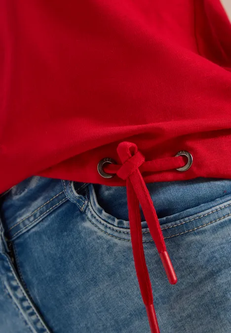 Roter Pullover mit Tunnelzug am Saum, kombiniert mit blauen Jeans.