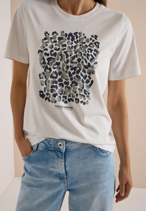 Kobieta w białym t-shircie z wzorem w panterkę i niebieskich dżinsach.