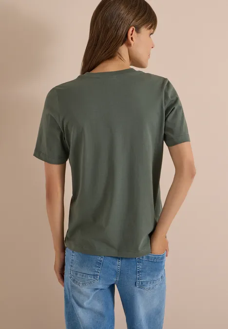 Kobieta widoczna od tyłu nosi khaki koszulkę i niebieskie jeansy.