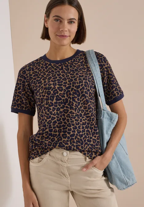 T-Shirt mit Rundhals und Leo-Muster creamy mocha Frau trägt kurzärmeliges Leopardenmuster-Shirt, helle Hose und blaue Tasche, lächelt vor neutralem Hintergrund.