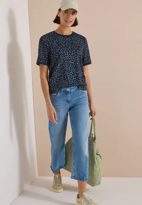 T-Shirt mit Rundhals und Leo-Muster dried olive green Frau in lässigem Outfit: Gemustertes T-Shirt, weite Jeans, beige Sneaker und Cap, mit grünem Stoffbeutel.