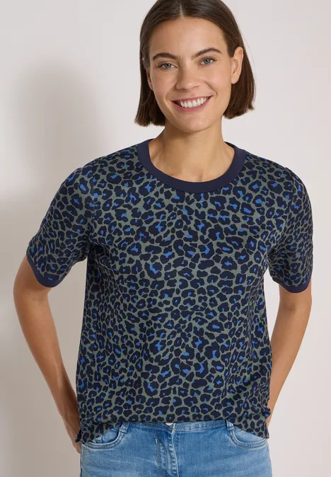 T-Shirt mit Rundhals und Leo-Muster dried olive green Frau mit kurzärmeligem Leo-Pullover in Blau-Grau, lächelnd vor hellem Hintergrund.
