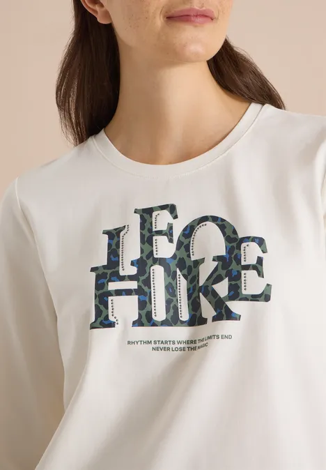 T-shirt à manches 3/4 avec inscription, style léopard vanilla white Frau trägt weißes T-Shirt mit großem Camouflage-Schriftzug 'LEGO HIKE'.