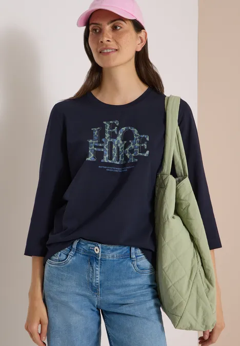 T-shirt à manches 3/4 avec inscription, style léopard urban dark blue Frau mit rosa Cap, dunkelblauem Langarmshirt mit 'HIKE'-Aufdruck, Jeans und grünem Stepp-Shopper.