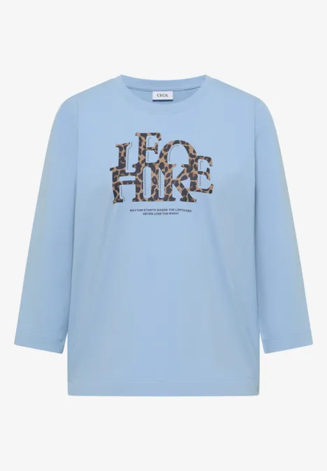 T-shirt à manches 3/4 avec inscription, style léopard easy blue Hellblaues Shirt mit 3/4-Ärmeln und braun-schwarzem Animal-Print-Schriftzug vorn.