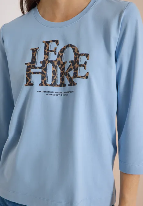 T-shirt à manches 3/4 avec inscription, style léopard easy blue Nahansicht eines hellblauen Shirts mit 3/4-Ärmeln und auffälligem 'LEO HIKE'-Schriftzug im Leopardenmuster.