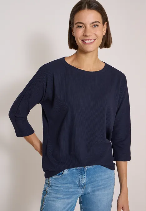 3/4-Arm Shirt mit Waffelstruktur urban dark blue Eine Frau mit kurzem braunem Haar trägt ein dunkelblaues Shirt und Jeans, sie lächelt.