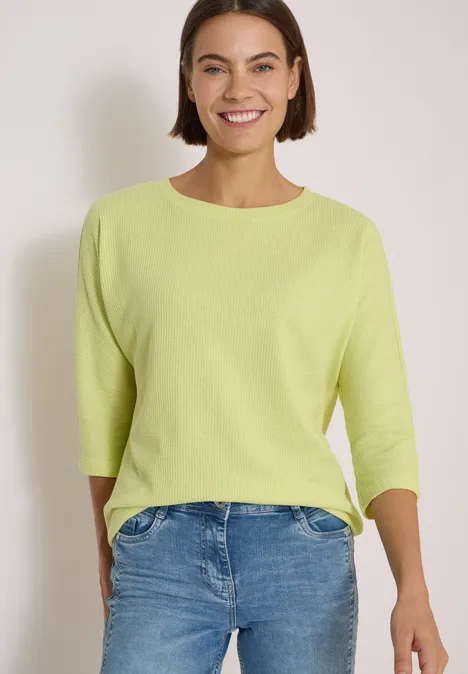 3/4-Arm Shirt mit Waffelstruktur citrin green Eine lächelnde Frau trägt einen hellgrünen Pullover mit 3/4-Ärmeln und blaue Jeans vor neutralem Hintergrund.