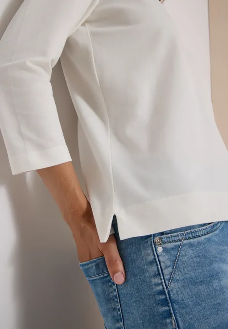 3/4-Arm Poloshirt mit Knopfdetail vanilla white Frau trägt weißes Shirt mit 3/4-Ärmeln und blaue Jeans, Hand in Hosentasche.