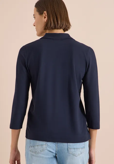 Rückansicht einer Person in dunkelblauem 3/4-Ärmelshirt und heller Jeanshose.
