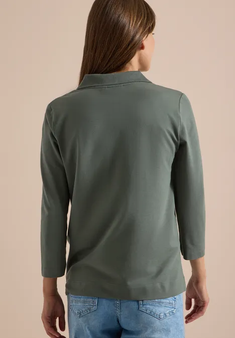 Polo à manches 3/4 avec boutons décoratifs dried olive green Frau von hinten in olivgrünem Langarmshirt mit Stehkragen und blauen Jeans.