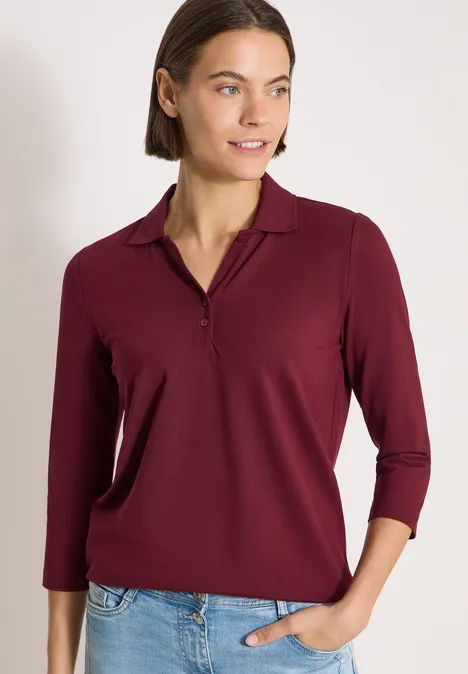 3/4-Arm Poloshirt mit Knopfdetail red wine Eine Frau trägt ein burgunderfarbenes Langarmshirt und Jeans, steht vor neutralem Hintergrund.