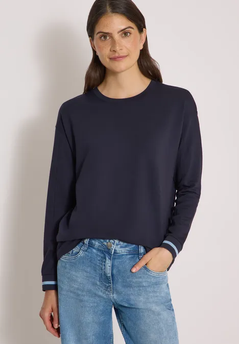 T-shirt à manches longues, col rond et rayures urban dark blue Frau in dunkelblauem Langarmshirt und Jeans vor hellem Hintergrund