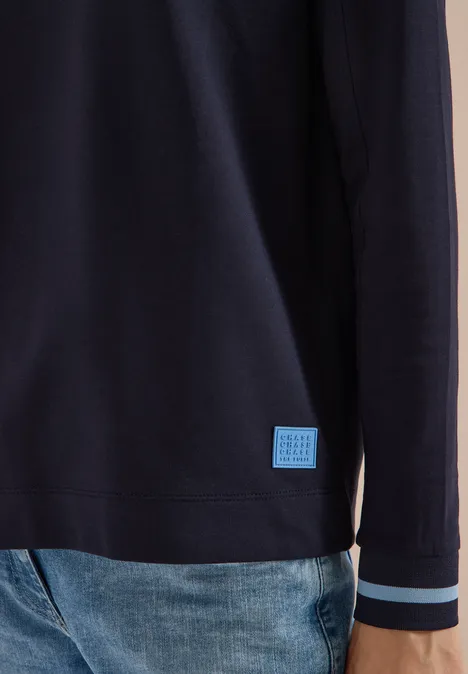 T-shirt à manches longues, col rond et rayures urban dark blue Dunkelblauer Pullover mit hellen Streifen an den Bündchen und kleinem Logo-Patch am Saum, kombiniert mit Jeans.