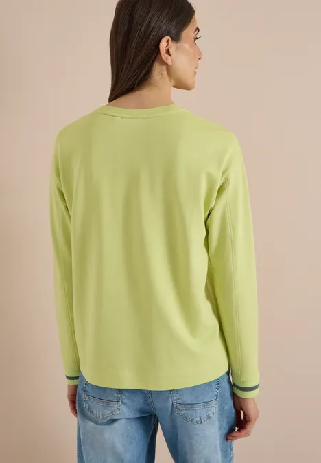 T-shirt à manches longues, col rond et rayures citrin green Eine Frau von hinten trägt eine grüne Langarmbluse vor beigem Hintergrund.