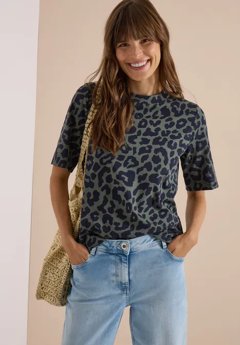 Lächelnde Frau in Leopardenmuster-Shirt, Jeans und Stroh-Tasche