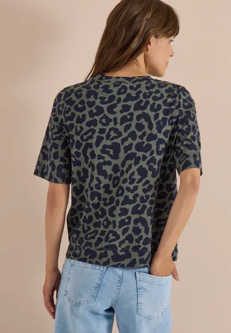 Frau von hinten in lockerem, kurzärmligem T-Shirt mit grünem Leopardenmuster und blauen Jeans.