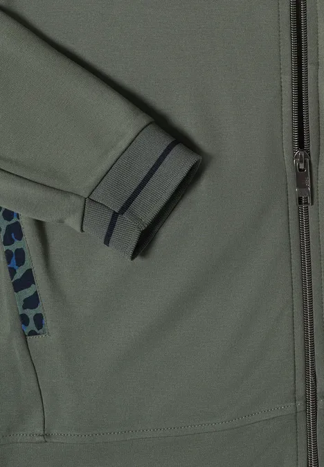 Nahaufnahme einer grau-grünen Jacke mit Reißverschluss, elastischem Ärmelbündchen und gemustertem Taschenbesatz.